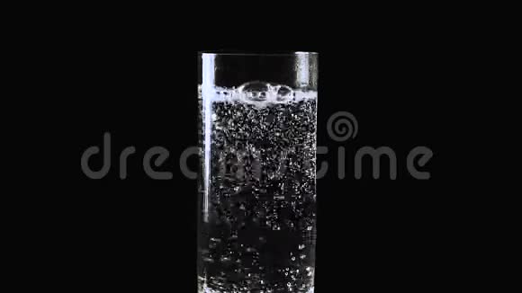 从矿泉水中慢慢地冒出泡沫在黑色背景的玻璃杯里放上苏打水视频的预览图