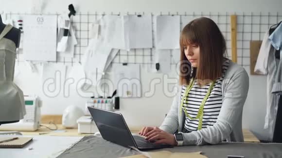 年轻的自雇裁缝正在使用笔记本电脑与客户沟通背景中的光现代工作室视频的预览图