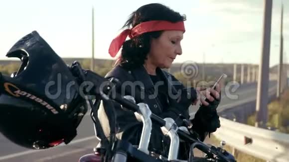 穿着皮夹克和手套的比基尼女人坐在他酷的摩托车上可见挂在方向盘头盔上A视频的预览图