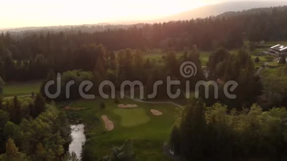 一个高尔夫球场的航拍镜头坐落在一片常绿森林里高尔夫球手在球道和果岭上打球视频的预览图