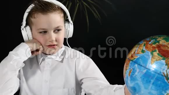 学校观念可爱的男孩坐在一张桌子上桌子上有地球仪后面有一块黑板无聊的男生绕地球转视频的预览图