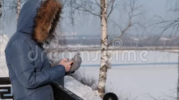 穿着蓝羽绒服的女人在冬天公园的手机里写短信侧视图视频的预览图