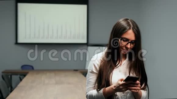一个穿着办公室服装的漂亮女孩站在会议室里戴着眼镜在手机上说话的肖像视频的预览图