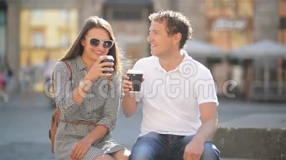 在阳光明媚的夏日里在城市广场的长凳上坐着一对喝咖啡的户外肖像视频的预览图