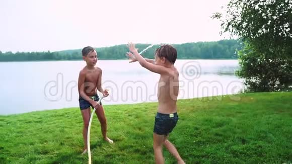 夏天男孩的泳裤向弟弟泼水弟弟在湖边的草地上玩得很开心视频的预览图