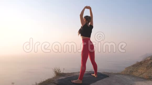 美丽的景色女人做瑜伽伸展在山上日落时的海景把手举起来视频的预览图