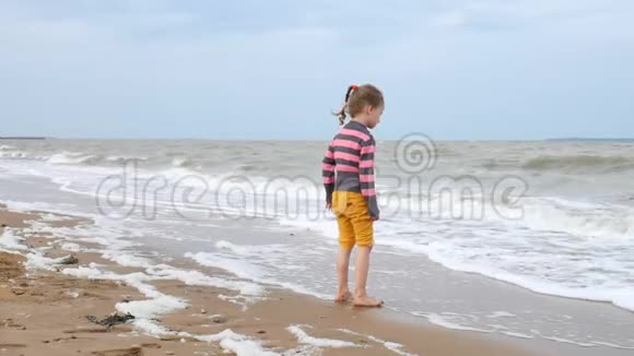 可爱的女孩看着大海中的波浪站在水边海上风暴强风巨浪视频的预览图
