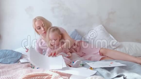 可爱的金发小女孩和她美丽的妈妈躺在床上画笔穿着粉红色的衣服视频的预览图