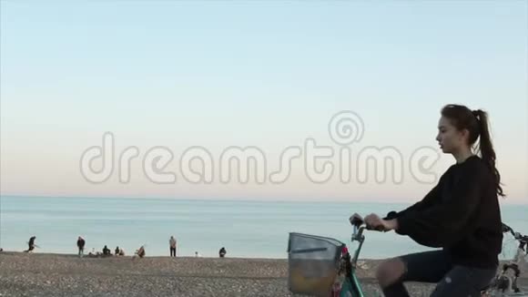 少女正骑着自行车在海边的沙砾滩上度过傍晚视频的预览图