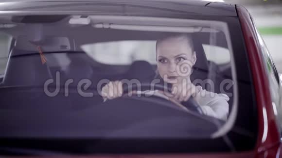 扎着马尾辫的年轻女子坐在红色的车里摇着头在方向盘后面视频的预览图