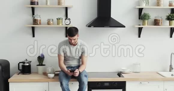 智能手机男人在家厨房的手机上浏览英俊的年轻人在智能手机上浏览微笑着快乐视频的预览图