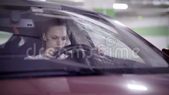 紧张可爱的女人穿着白色衬衫坐在方向盘后面的红色汽车里视频的预览图