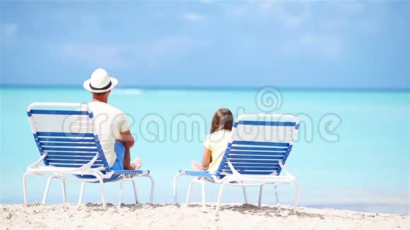 父亲和女儿坐在沙滩上的躺椅上视频的预览图