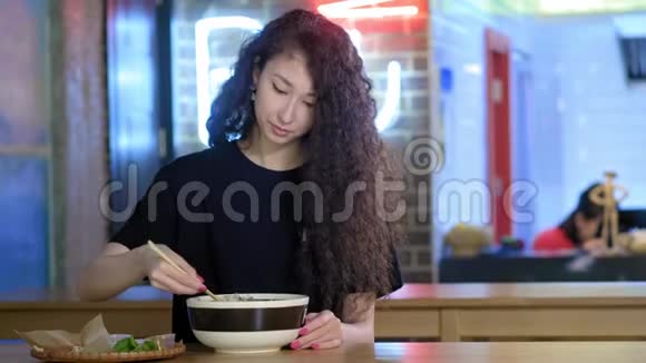 一个可爱的年轻亚洲女孩正在亚洲咖啡馆里吃PHO汤用中国筷子吃面条中文视频的预览图