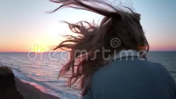 美丽的白种人卷曲的金发年轻女子在日出或日落海边风发了头发她呼吸视频的预览图