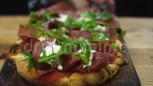 提供美味的意大利小比萨沙拉培根和奶油奶酪放在桌子上方的木铲上视频的预览图