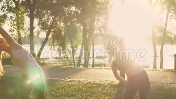 两名年轻女子在公园做有氧运动减肥健身模式锻炼日落和自然背景视频的预览图