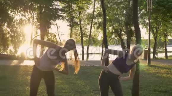两位年轻女子在公园里做有氧运动减肥健身模特运动镜头耀斑和美丽的景色视频的预览图