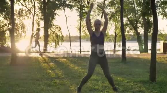 年轻漂亮的女人在公园做明星运动减肥健身模特跳跃其他女人在后面跑步镜头视频的预览图