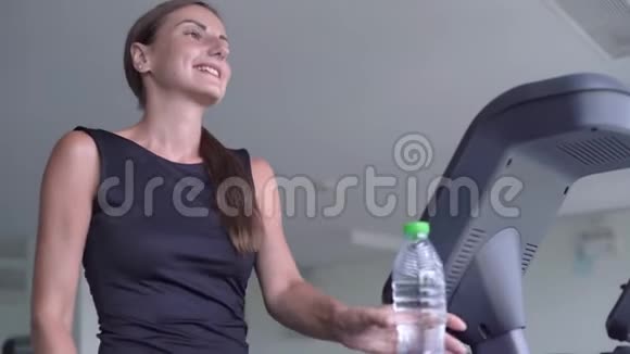 漂亮的健身女孩在健身房跑步机上跑步和喝水视频的预览图