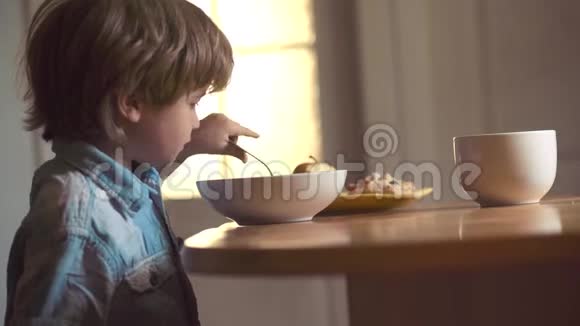 快乐的小男孩勺子吃自己小男孩坐在桌子旁吃牛奶零食宝宝在厨房吃食物视频的预览图