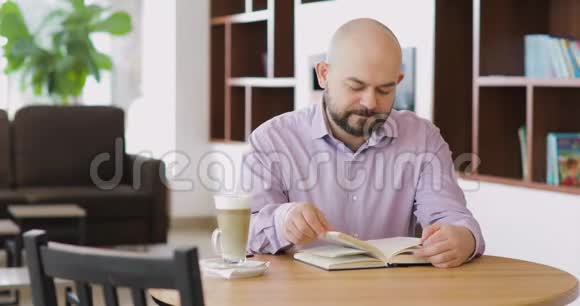男人正在看一本书坐在酒店大厅的咖啡馆里喝着一杯卡布奇诺视频的预览图