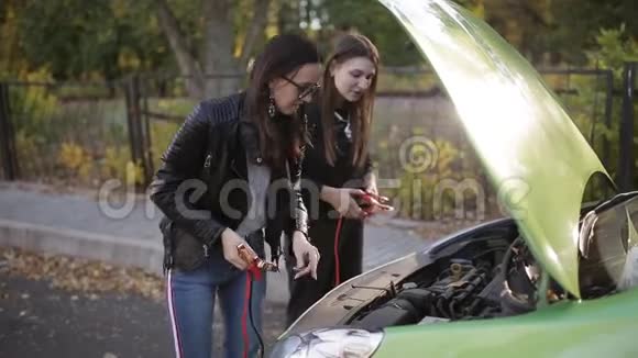 两个不太聪明的女孩试图给一辆死车充电两个女孩在一辆车的敞篷前试图连接视频的预览图