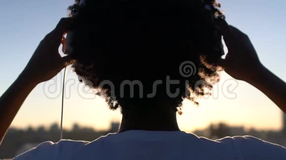 卷发女人戴上耳机享受神奇时刻的剪影视频的预览图