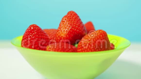 在蓝色背景的绿色碗里放着红色多汁的草莓在一个圆圈里旋转视频的预览图