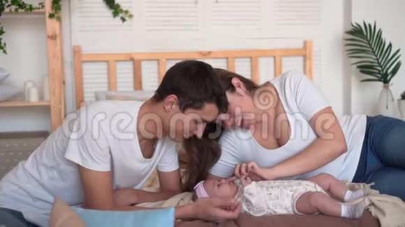 微笑的家庭在床上爸爸和妈妈正在看触摸和谈论他们的宝贝女儿视频的预览图