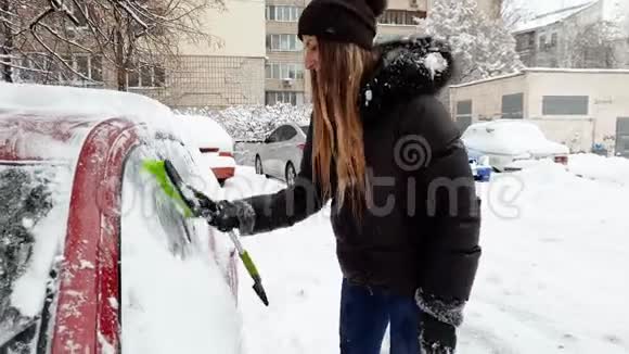 4k视频美丽微笑的年轻女子用伸缩刷子从雪中清洁汽车视频的预览图