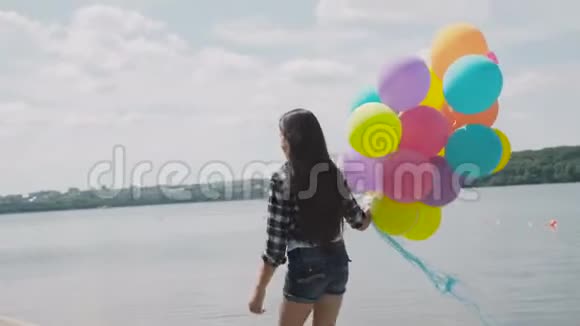 快乐的女孩走着摆着五颜六色的气球在湖岸上视频的预览图