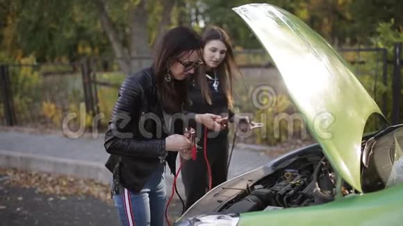 两个不太聪明的女孩试图给一辆死车充电两个女孩在一辆车的敞篷前试图连接视频的预览图