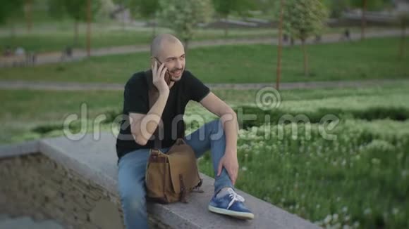 一个夏天的下午迷人的男性坐在城市公园里打电话视频的预览图