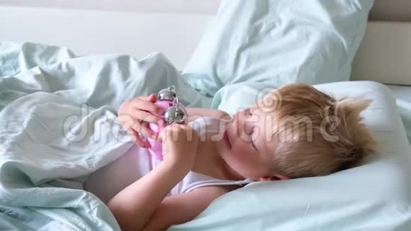 一个金发小男孩躺在床上微笑一大早就玩闹钟那男孩听着钟响视频的预览图