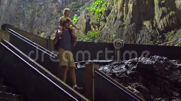 父亲把儿子挂在肩膀上走在马来西亚巴图古洞里的楼梯上那里有一个印度教视频的预览图