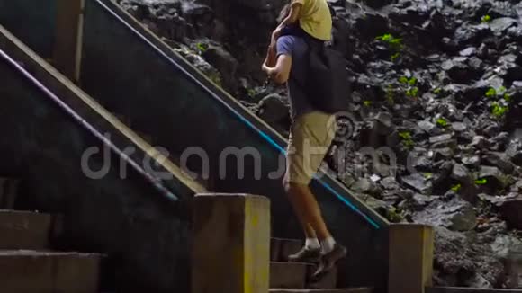 父亲把儿子挂在肩膀上走在马来西亚巴图古洞里的楼梯上那里有一个印度教视频的预览图