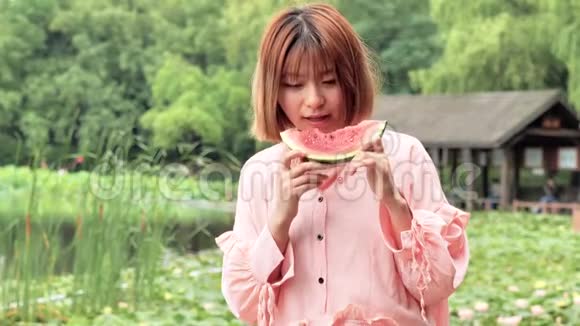 夏天的女人吃西瓜片微笑着在公园里吃西瓜的中国女孩假日生活方式夏季概念视频的预览图