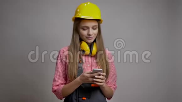 年轻漂亮的女孩建设者正在展示她的智能手机的彩色屏幕微笑沟通概念灰色背景视频的预览图
