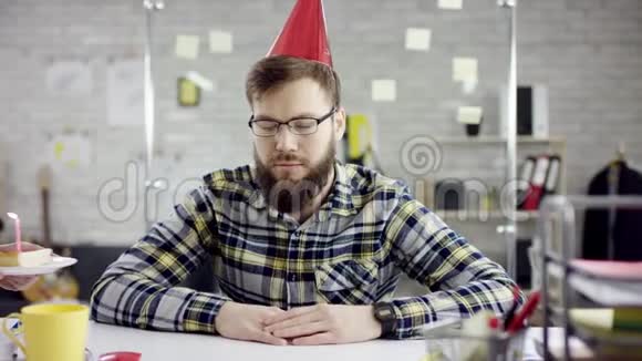 悲伤的胡子商人办公室工作人员正在办公室里庆祝一个孤独的生日他在一个小蜡烛上吹蜡烛视频的预览图