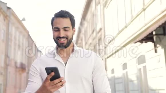 微笑的男人用手机在城市大街上散步视频的预览图