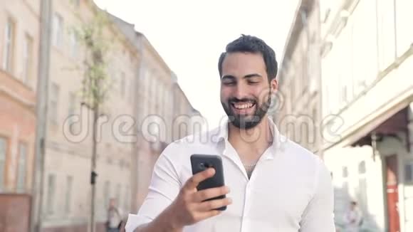 微笑的男人用手机在城市大街上散步视频的预览图