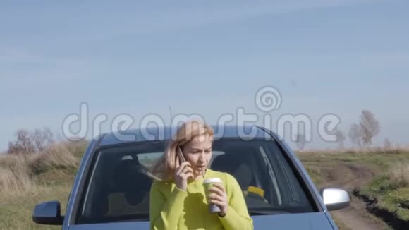 一位自信的年轻女商人在车旁端着一杯咖啡正在打电话4公里视频的预览图