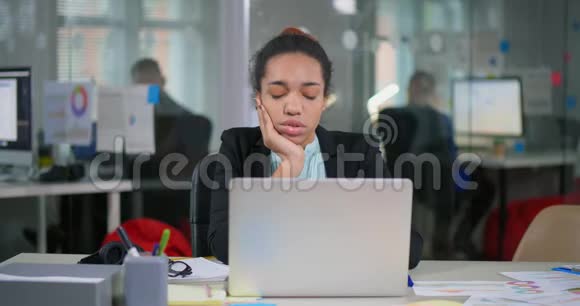 非洲无聊的女人坐在办公室的笔记本电脑前视频的预览图