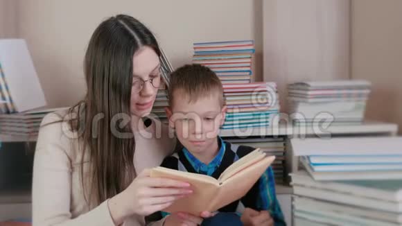 妈妈戴着眼镜给坐在书中间的儿子读一本书视频的预览图