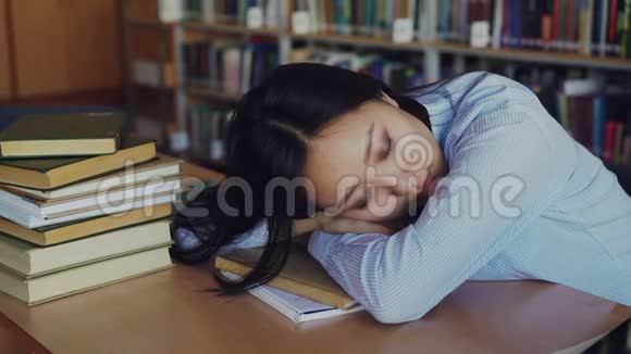 年轻漂亮疲惫的亚洲女学生正坐在书桌前头靠在桌子上她正睡在课本上视频的预览图