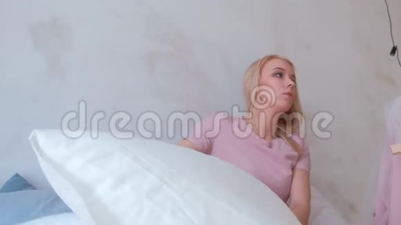 年轻迷人的金发妈妈和她穿着粉红色裙子的迷人小女儿玩女孩落在枕头里视频的预览图