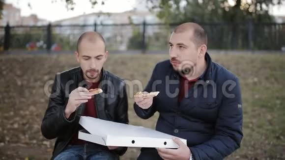 两个男人的朋友坐在公园的长凳上从盒子里吃披萨视频的预览图