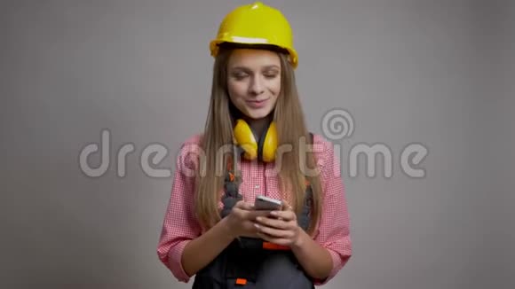 年轻漂亮的女孩建设者正在展示她的手机的色度屏幕微笑沟通的概念灰色背景视频的预览图