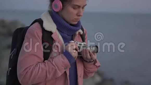 戴着耳机的女孩在她的老式相机上拍下了大海日落的照片视频的预览图
